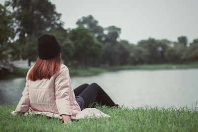 Rear view of woman sitting on grass by lake