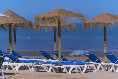 Lounge chairs and parasols on beach against blue sky