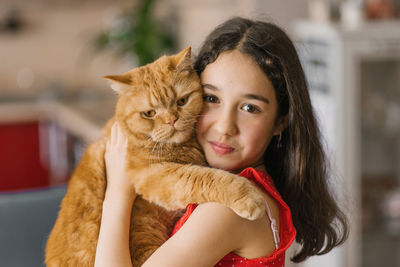Child girl holds her pet red british cat in her arms and sits with him on the couch at home