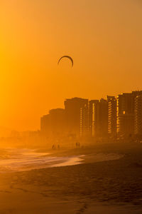 Silhouette city by sea against clear sky during sunset