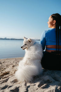 Woman with locs sitting on the beach of city lake with her best friend, snow-white japanese spitz