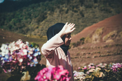 Woman gesturing while standing amidst flowers against mountains