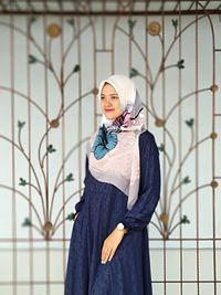 Portrait of young woman standing against wall