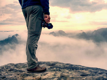 Photographer hand with camera, legs, knees and boots. man takes landscape photos of dreamy fall 