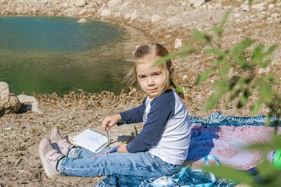 Young girl enjoying a peaceful day by the serene lake, immersed in her art and creativity