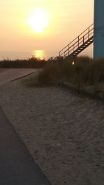 Footpath by road against sky during sunset