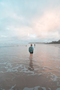 Rear view of woman standing at beach against sky