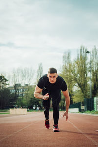 Portrait of young man running on sports track against sky