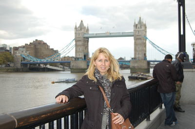 Portrait of woman standing by railing against tower bridge