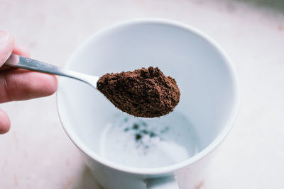 Cropped hand pouring ground coffee in mug at home