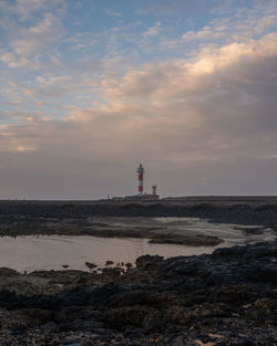 Lighthouse on beach by sea against sky