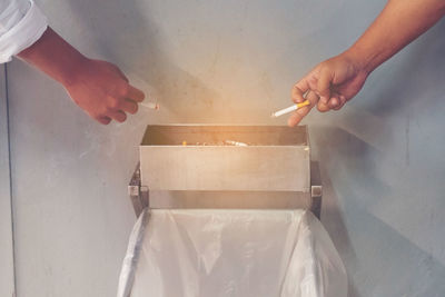 Cropped image of hands throwing cigarette in container