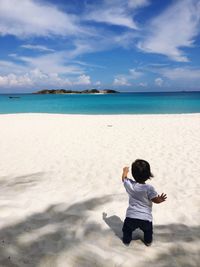 Rear view of baby boy standing on sand at beach against sky