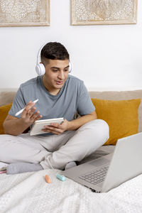 Young man with casual clothes sitting on the bed at home with laptop computer and studying