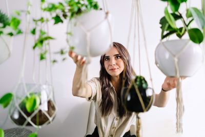 Portrait of beautiful young woman holding potted plants at home