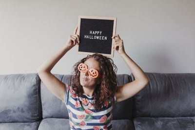 Portrait of woman in novelty glasses holding happy halloween text at home