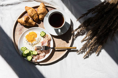 Breakfast in bed coffee cup, fried egg, bacon and croissants on wooden tray. 