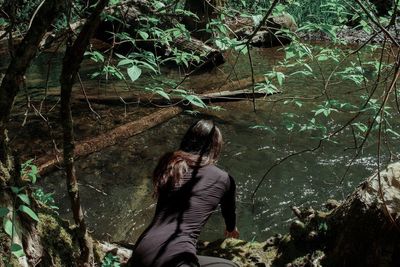 Rear view of woman touching water in pond at forest