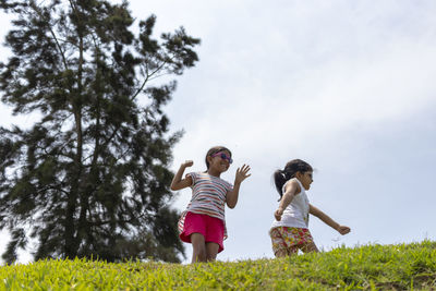 Low angle view of sisters playing on grass against sky