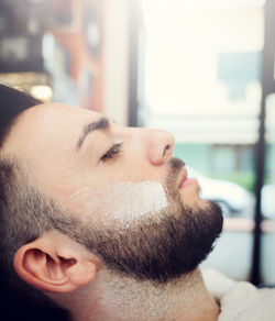 Man with shaving cream on face sitting in barber shop