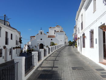 Narrow road amidst whitewashed buildings in village of mijas against clear blue sky in spain.
