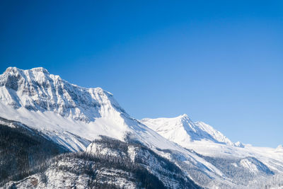 Low angle view of snowcapped mountains against clear blue sky