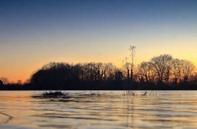 Silhouette trees by lake against sky during sunset