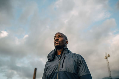 Low angle view of male athlete looking away while standing against cloudy sky