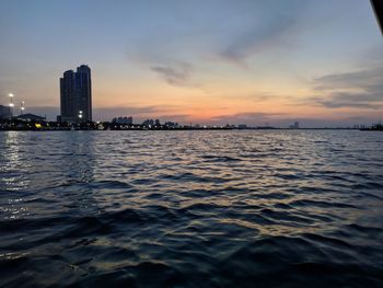 Scenic view of sea by buildings against sky during sunset