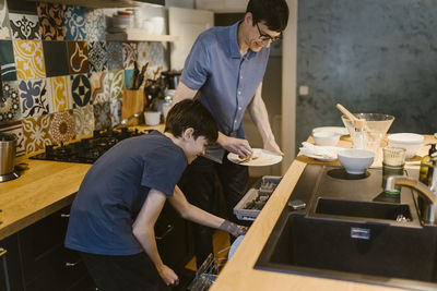 Father and son putting dishes in dishwasher after dinner at home