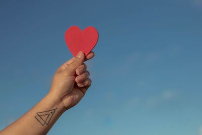 Cropped hand of woman holding heart shape against sky