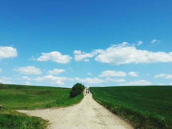 Country road amidst grassy field against sky