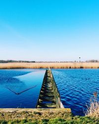 Pier on lake against clear blue sky
