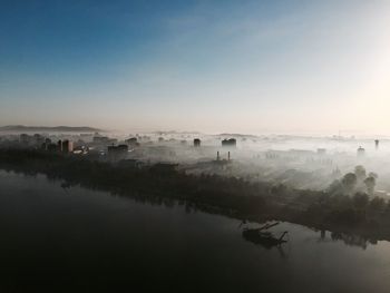 Cityscape by river against sky in foggy weather