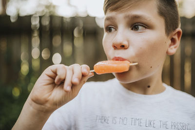 Close-up of thoughtful boy sucking popsicle at backyard during summer