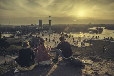 People sitting in city against sky during sunset