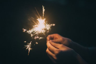 Cropped hands holding sparkler against black background