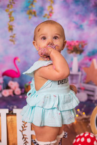 Portrait of cute baby girl standing eating birthday cake