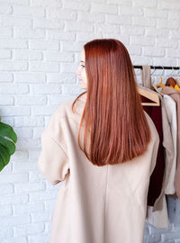 Beautiful young woman in beige coat standing in front of hanger rack and choosing outfit dressing