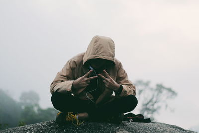 Rear view of man sitting in front of built structure against sky