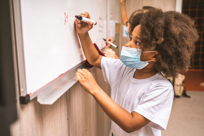 Cute girl wearing mask writing on whiteboard