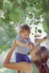 Cute smiling woman with arms raised against trees