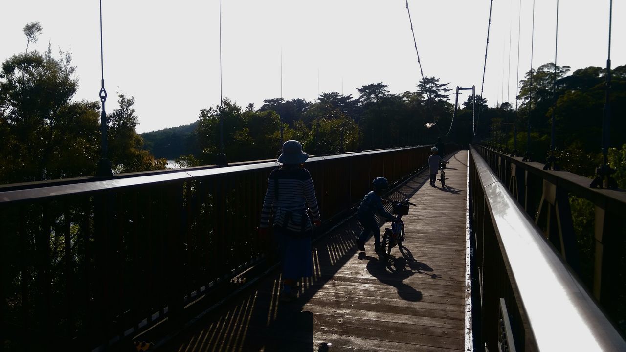 REAR VIEW OF PEOPLE RIDING ON FOOTBRIDGE