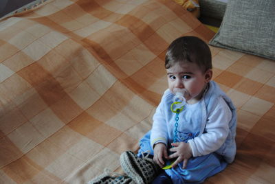 Portrait of cute baby boy with pacifier in mouth sitting at home