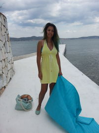 Portrait of young woman with textile standing on pier by sea