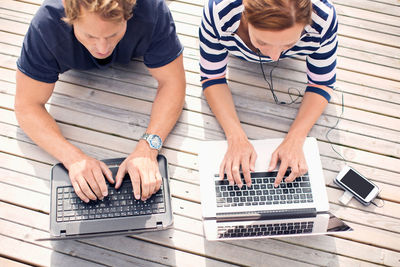 High angle view of mature couple using laptops while lying on pier