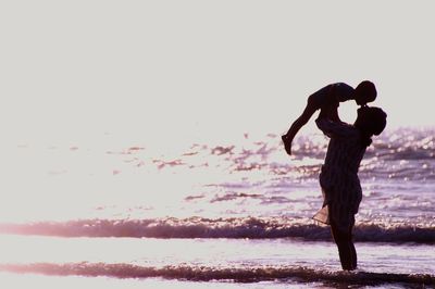 Woman standing at beach against sky during sunset