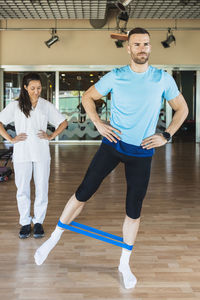 Sportsman with hands on hips exercising with resistance band in gym