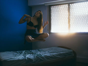 Woman levitating over bed at home during sunset