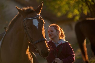 Girl stroking horse while standing in barn during sunset